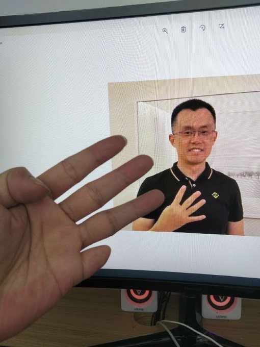 A hand obscures part of a screen displaying a man in a black shirt with the Binance logo and a text overlay with what appears to be a Chinese advertisement for a "digital coin" and "trading".