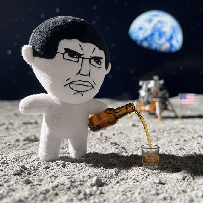 A plush toy with a grumpy man's face pours brown liquid from a bottle into a small glass on the surface of the moon, with Earth visible in the background and a lunar lander with an American flag nearby.