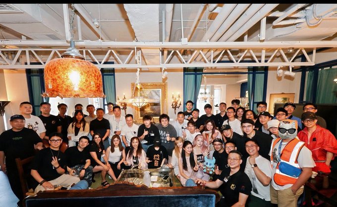 A large group of around 40 people pose together for a group photo at an indoor venue in Shanghai, including someone in a furry mascot costume. The post notes this captures "some of the apes" who attended their 8-hour Shanghai event hosted by the Bored Ape Yacht Club.