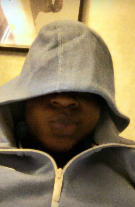 A close-up selfie of a person wearing a light blue hoodie pulled up over their head, casting a shadow over their eyes.