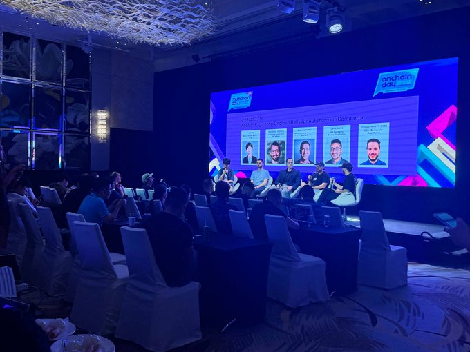 A conference event labeled 'onchain day' featuring a panel discussion on 'The Road to Mass Onchain Adoption and Economic Commerce,' with four speakers seated on stage in front of an audience.