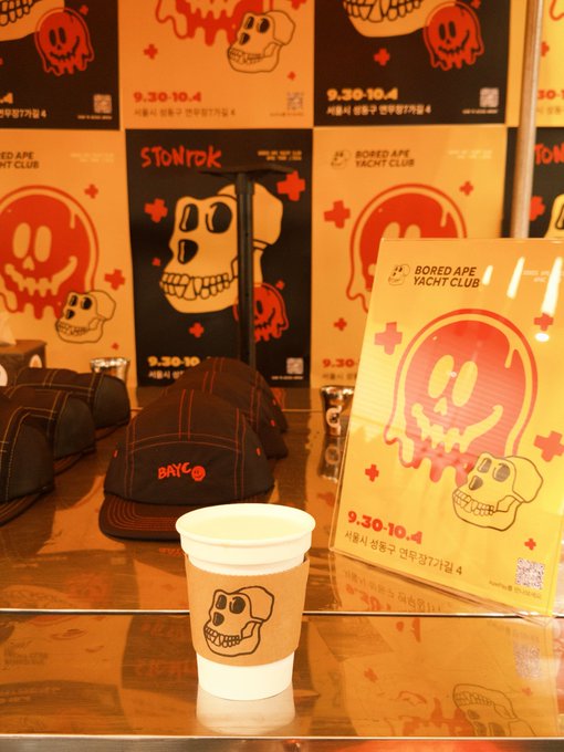 A display for the 'Bored Ape Yacht Club' x 'STONE TDK' collaboration (9.30-10.4) features skull and ape graphics on posters, branded baseball caps, and a paper cup.