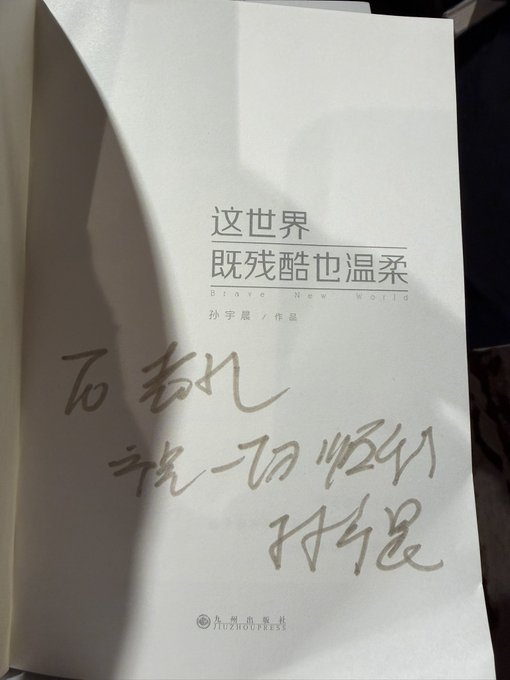 A Chinese book titled '这世界既残酷也温柔' (Brave New World) by 孙宇晨 (Justin Sun) with handwritten Chinese calligraphy on the inside page.