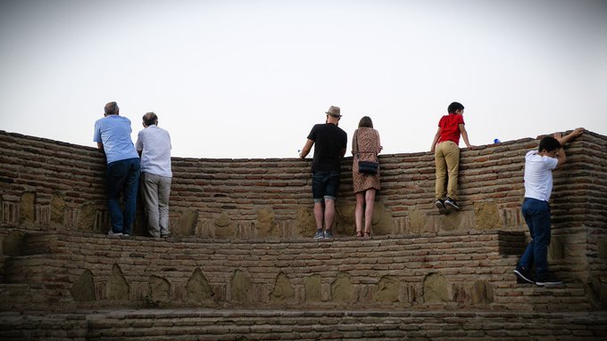 Several people standing on a curved brick wall looking out toward a hazy horizon.