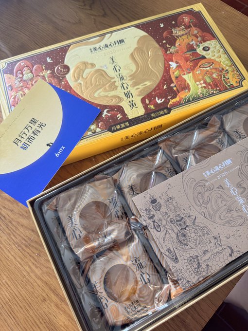 A box of mooncakes (月餅) from 美心 (Maxim's), showing the ornate gold and red packaging featuring traditional artwork, opened to reveal individually wrapped pastries inside.