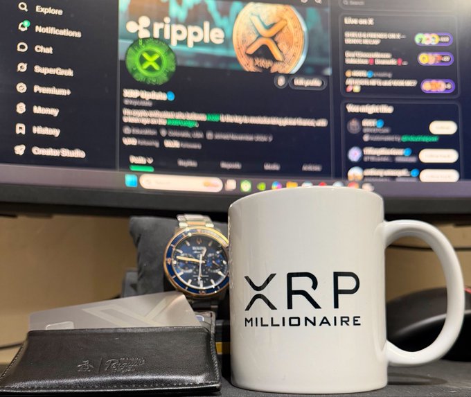 A white "XRP MILLIONAIRE" mug sits on a desk next to a luxury watch and wallet, with a monitor displaying the Ripple (XRP) Twitter profile in the background. The setup perfectly captures the optimistic vibe of the post celebrating being an XRP holder with a morning coffee.