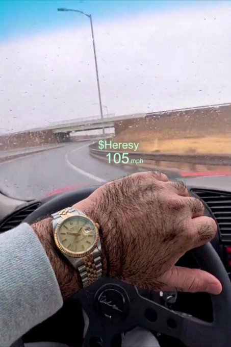 A driver's perspective shot showing a hairy hand wearing a gold and silver Rolex-style watch on the steering wheel, with a Snapchat filter overlay reading '$Heresy 105 mph' on a rainy highway.