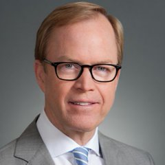 A man with light brown hair wearing rectangular black glasses, a gray suit, white shirt, and light blue striped tie smiles at the camera in a professional headshot against a gray background. The image appears to accompany news about Jurrien Timmer, Fidelity's Director of Global Macro, who is shown making bullish predictions for Bitcoin's long-term price target.