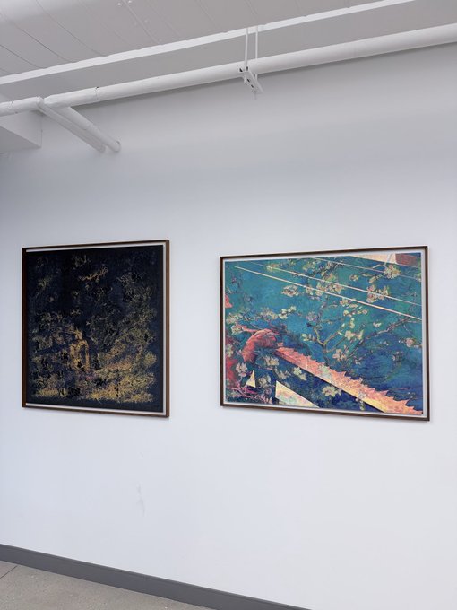 Two framed paintings hang side by side on a white gallery wall beneath exposed pipes, depicting dark forest scenes with trees rendered in contrasting dark and blue-toned palettes.
