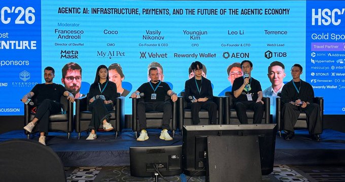 A panel of seven people sit on stage at the HSC'26 conference, with the screen behind them displaying "AGENTIC AI: INFRASTRUCTURE, PAYMENTS, AND THE FUTURE OF THE AGENTIC ECONOMY" and identifying the participants as moderator Francesco Andreolí (Director of DevRel, MetaMask), Coco (CMO, My AI Pet), Vasiliy Nikonov (Co-Founder & CEO, Velvet), Youngjun Kim (CPO, Rewardy Wallet), Leo Li (Co-Founder & CTO, AEON), and Terrence (Web3 Lead, TIDB). The image illustrates the panel being referenced in the post about AI agents' payment infrastructure.