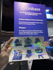 A hand holds Unibase stickers featuring "Intelligent Agent Starter" designs in front of a booth banner promoting "The Decentralized Memory Layer for AI," aligning with the post about showcasing Based Memory at the Base APAC Pavilion during Malaysia Blockchain Week.