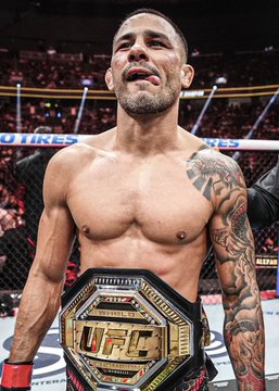 UFC fighter Alex Pereira posing shirtless with a bleeding cut above his eye, wearing the UFC championship belt around his waist in the octagon.