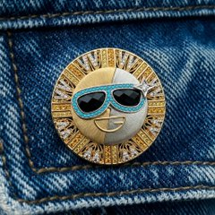 A sun-faced enamel pin wearing blue sunglasses is pinned to a denim background, complementing the post’s discussion of SUN token’s rising 13.41% trading volume, $17.955 million 24-hour volume, and $329.46 million market cap.