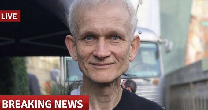 A close-up of an older man with white hair and blue eyes, framed by 'LIVE' and 'BREAKING NEWS' banners.