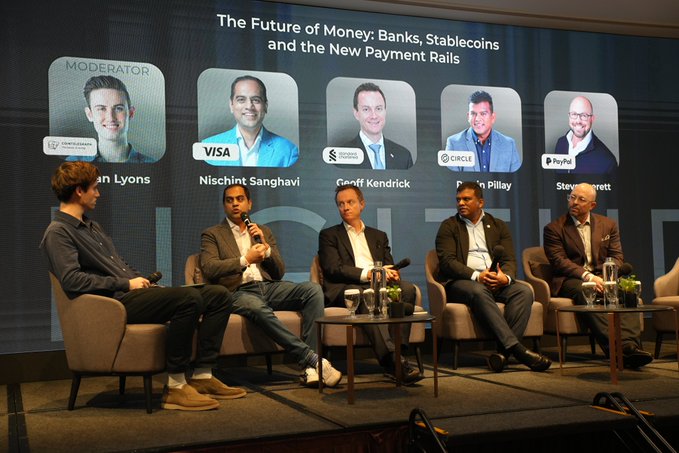 Five men sit in a row of tan armchairs on a stage at the "The Future of Money: Banks, Stablecoins and the New Payment Rails" panel at LONGITUDE Singapore, with a large screen behind them displaying the event title and headshots of moderator Ciaran Lyons alongside panelists from Visa, Standard Chartered, Circle, and PayPal.