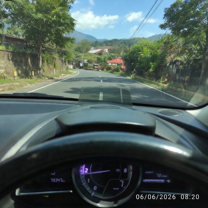 A car's GPS navigation system displays information about a street called "Rivers" with an estimate of the time remaining at 8:20 am, as well as information about the altitude of a mountain and other nearby landmarks like "Wallchain". The photo is taken from the perspective of someone driving down the road in front of these landmarks.