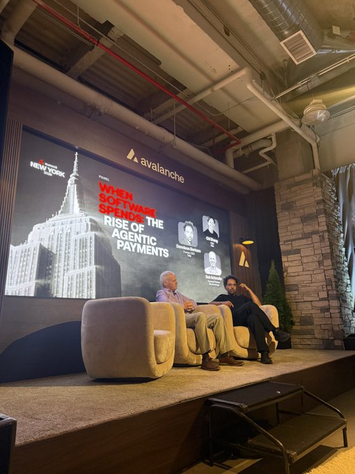 Two men sit on a small stage with cream-colored armchairs in front of a large screen displaying the Avalanche logo, a 'New York' Magazine panel titled 'When Software Spends The Money: Rise Of The Agentic Payments' featuring the Empire State Building, and photos of speakers Jonathan Brassington and Anil Dharni.