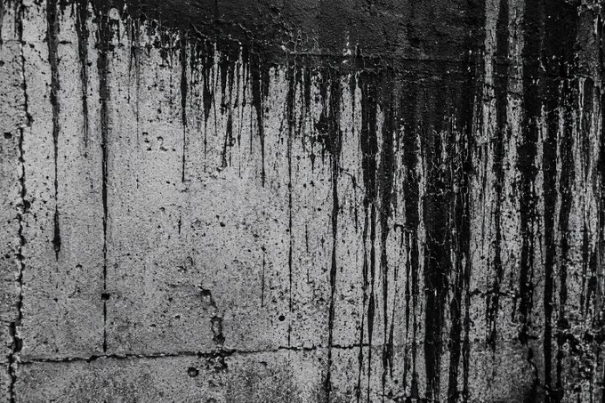 A black-and-white photograph of a wall with dark streaks dripping down, resembling paint drips or water stains, with the number "52" faintly visible on the left side.