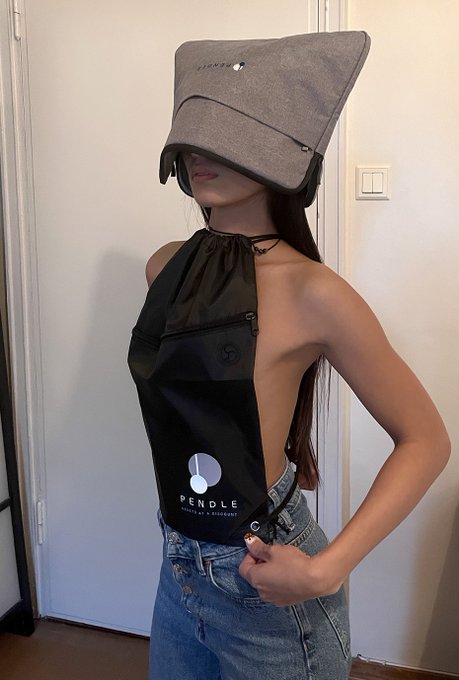 A woman models a unique fashion item that combines a gray hat with a black drawstring backpack bag, featuring the text "PENDLE" and "BUILT TO ENDURE."