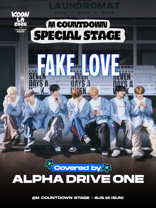 Promotional poster for KCON LA 2026 announcing Alpha Drive One's cover performance of "Fake Love" on the M Countdown Special Stage at Crypto.com Arena on August 16 (Sun). The image features seven members of the group seated on a couch in denim outfits in front of a laundromat backdrop.