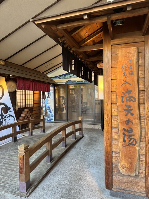 The entrance to a traditional Japanese onsen (hot spring bath) features a wooden archway with a large vertical sign reading "満天の湯" (Manten no Yu, meaning "Full Sky Bath"). The post about recovery from conference exhaustion and travel fatigue aligns with this image, as onsen visits are a popular way to relax and rejuvenate in Japan.