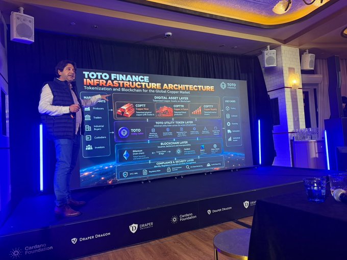 A man presenting on stage about 'TOTO FINANCE INFRASTRUCTURE ARCHITECTURE,' detailing tokenization and blockchain layers for the global copper market.
