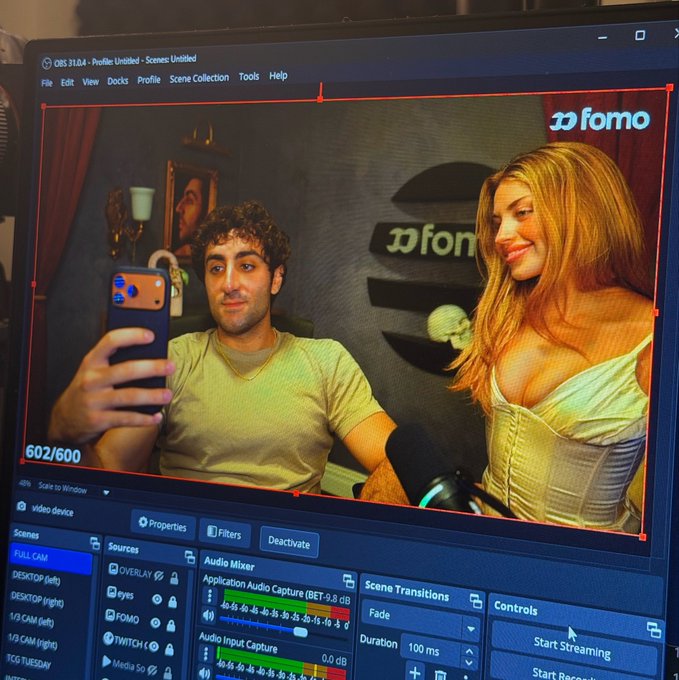 A computer screen displaying OBS streaming software with a preview of two people taking a selfie in front of a 'fomo' branded backdrop.