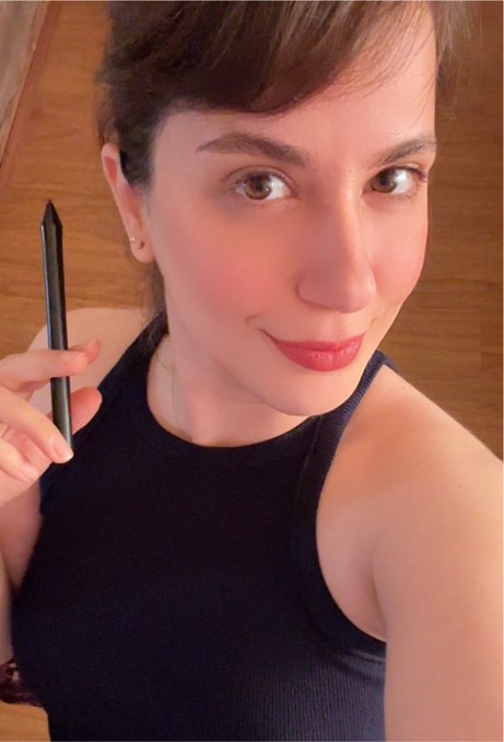 Selfie of a woman in a black tank top holding a black stylus pen, with long nails and red lipstick.