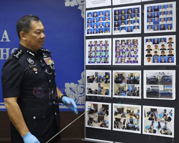 A Malaysian police officer points to a board displaying mugshots and evidence from dismantled scam operations, likely related to the text about Chinese nationals arrested for fraud in Johor. The image visually supports the accompanying post by showing law enforcement's efforts against criminal networks.