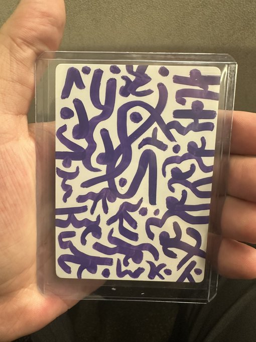 A hand holding a playing card in a clear plastic sleeve, featuring abstract purple squiggles and doodle-like designs on a white background.