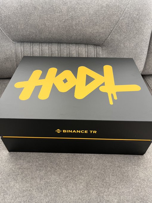 A black box with "HODL" written in yellow graffiti-style lettering and "BINANCE TR" printed near the bottom edge.