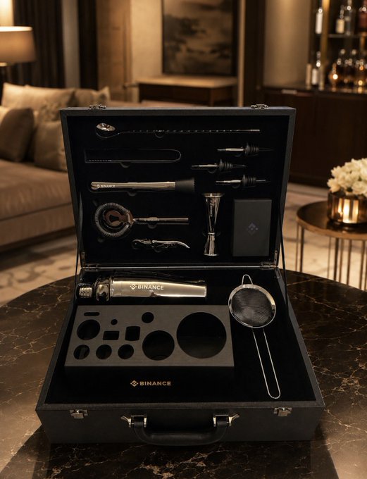 An open black carrying case displaying a branded 'Binance' barista kit with various coffee-making tools, including a tamper, stencils, and a strainer, sitting on a marble table in a luxurious lounge setting.