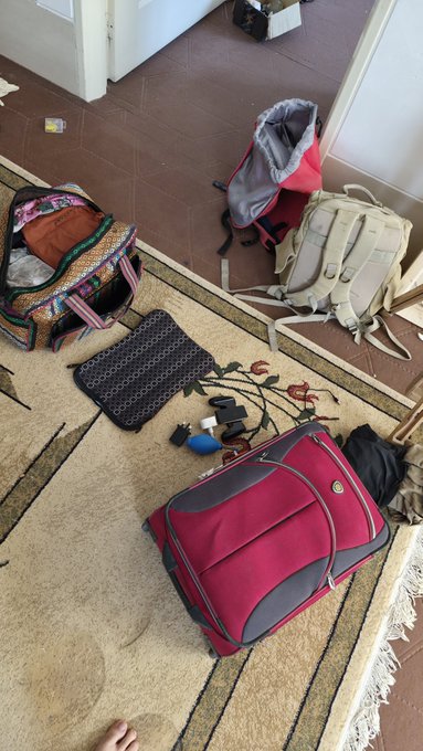 An overhead view of a room showing packed bags, luggage, and scattered belongings on a rug and tiled floor.