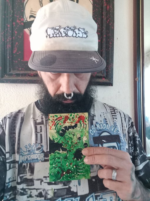 A bearded man wearing a cap with text "WEEDA" holds up a colorful pixel art card or sticker featuring green slime artwork, wearing a shirt that reads "IMPERADOR UNDERGROUND" and "OS NADA VÊ".