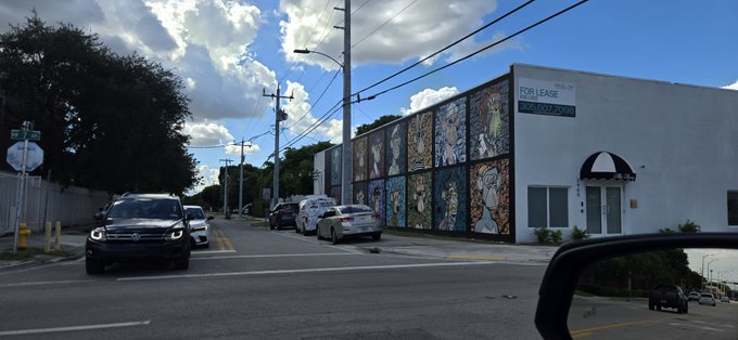 A street view shows a building with 'FOR LEASE' signs and colorful mural panels, with cars parked along the road under a cloudy blue sky.