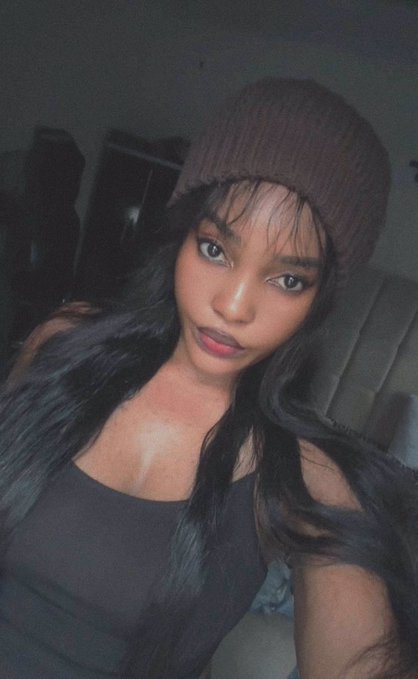 A young woman wearing a brown beanie and black top poses for a selfie in a dimly lit room, matching the relaxed late-night vibe of the "good night" message wishing followers rest before tackling another day of work on $River.