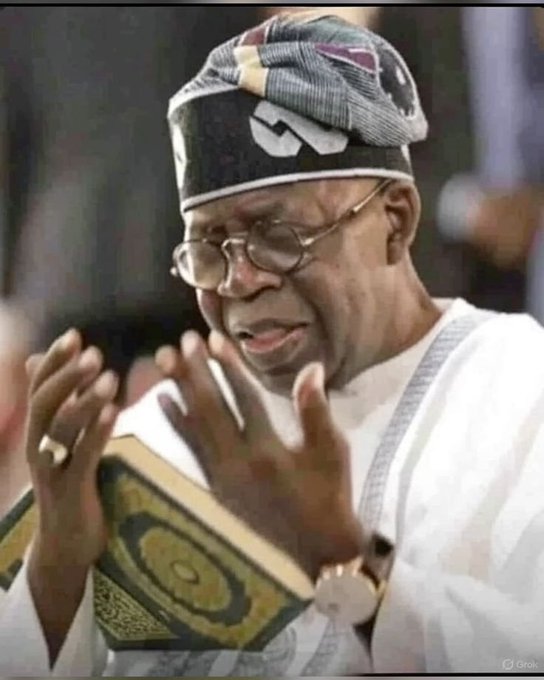A photograph of an elderly man wearing traditional Nigerian attire including a patterned cap and glasses, holding what appears to be a religious text while raising his hands.