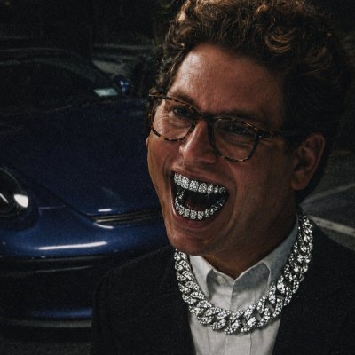 The post says "Gm everyone" — typically a casual morning greeting in online communities — paired with an image of a man laughing maniacally with diamond grills and an oversized diamond chain, in a style reminiscent of "Saltburn" (2023). The caption humorously contrasts the cheerful greeting with the unsettling, unhinged expression in the photo.