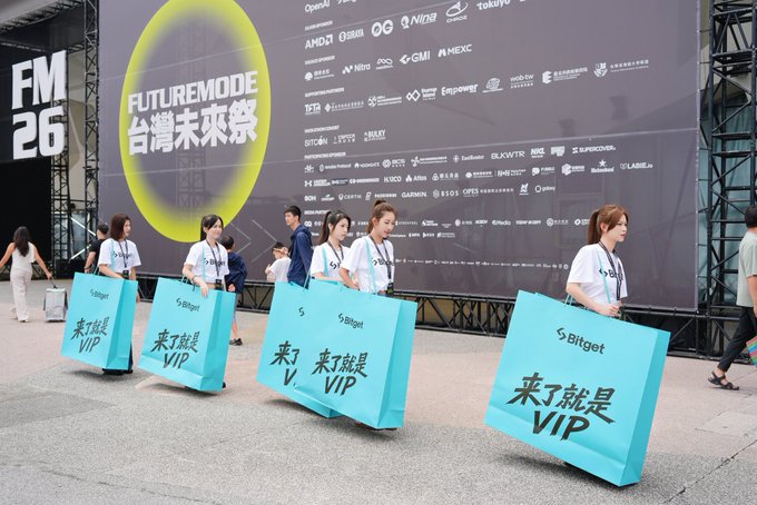 A group of people carry large teal shopping bags reading 'Bitget' and '來了就是 VIP' in front of a sponsor board displaying 'FUTUREMODE 台灣未來線' and various cryptocurrency and tech logos.