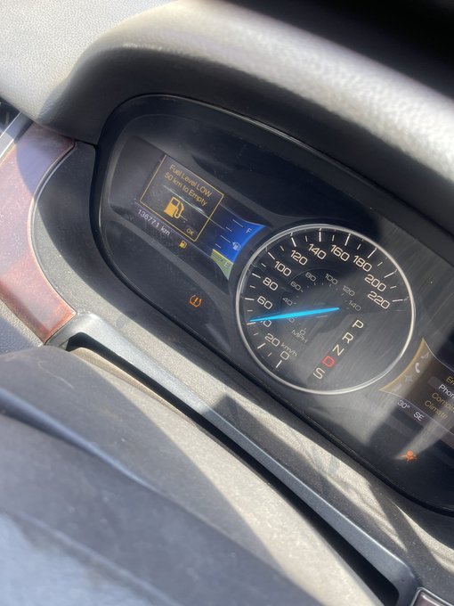 A vehicle's dashboard showing a speedometer and a digital display with a 'Fuel Level LOW' warning alert.