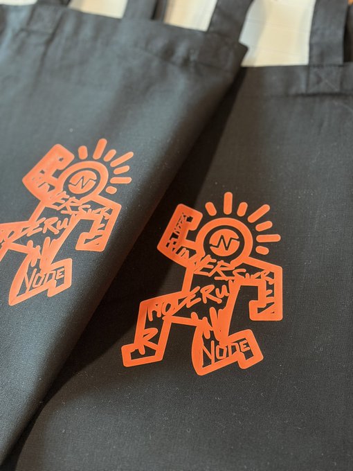 Close-up of black fabric featuring an orange graphic print of a figure with 'MODERUT NONE' and 'N' lettering.