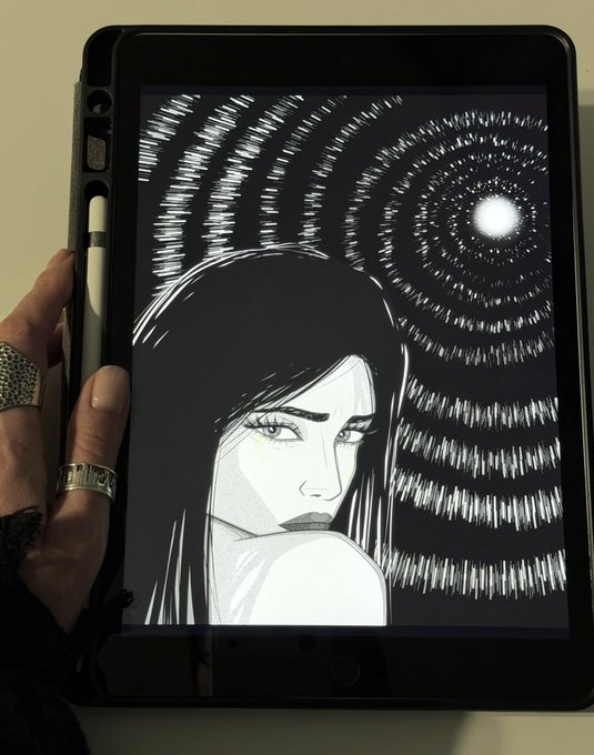 A hand with rings holds a tablet displaying a digital black and white drawing of a woman looking over her shoulder, with a swirling pattern of dots radiating behind her.