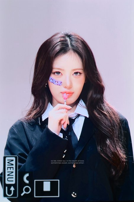 A young woman with long dark hair wearing a school uniform, holding a pink lollipop near her face with purple eye decorations, in what appears to be a K-pop concept photo with a 'MENU' overlay.
