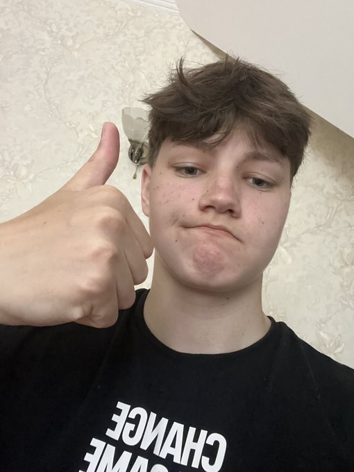 A young male wearing a black t-shirt with 'CHANGE' text (partially visible) gives an enthusiastic thumbs-up to the camera in a dimly lit room.