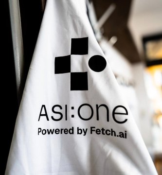 A close-up of a white shirt or banner displaying the 'ASI:One Powered by Fetch.ai' logo with a geometric icon.
