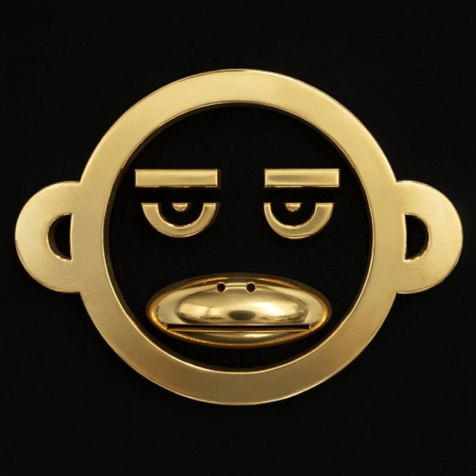 A 3D rendered golden Paul Frank monkey face emblem with droopy eyelids, a protruding muzzle, and round ears set against a black background.