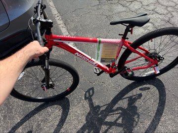 A red mountain bike with "SPECIALIZED" branding on the frame is held up on a paved street, presented as the bicycle purchased by AI—its solid, ready-to-ride appearance giving the claim a tangible, real-world feel.