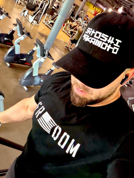 The image shows a man wearing a black baseball cap with white text that reads "I'm a Bitcoiner". He is standing inside a gym, surrounded by exercise equipment such as treadmills and weight machines. The caption above his head suggests he might be promoting or discussing the concept of cryptocurrency in relation to fitness and health.