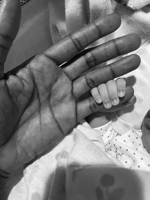A black and white close-up shows an adult hand cradling a tiny baby hand, highlighting the size contrast between the two.