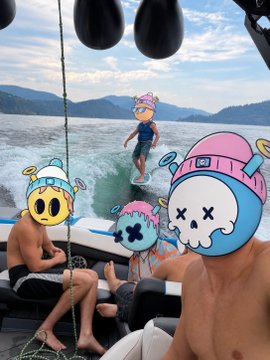 A photo of people on a boat with cartoon character stickers (smiley face, pink-haired figure, blue skull) edited over their faces, with one person wakeboarding behind the boat.